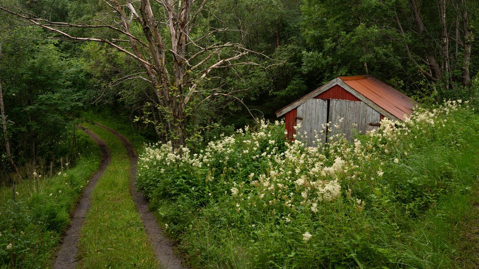A rural travel route winding past a weathered red building