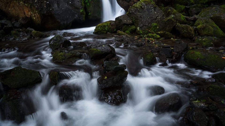 Fast water and mossy rocks near a waterfall